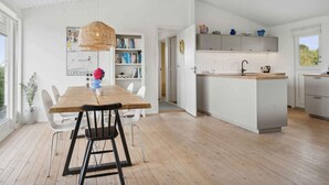 A modern kitchen with white cabinetry, a wooden island, and a dining area with a wooden table and chairs. - 5 Star Holiday Home in Bogense (Bogense)