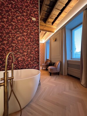 Une salle de bain moderne avec une grande baignoire, des poutres en bois au plafond et une vue sur l’extérieur grâce à une grande fenêtre.