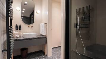 Une salle de bain moderne dotée d’un plan de toilette en granit, d’un grand miroir, d’une cabine de douche en verre et d’un porte-serviettes intégré.