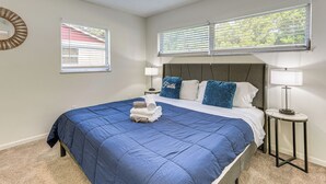 A bedroom with a large bed, two bedside tables with lamps, a window with blinds, and a wall clock. - Gateway to Orlando Theme Parks! Home w/ Large Yard (Winter Park)