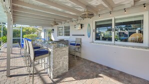 A covered outdoor seating area with wicker chairs, a stone table, and a surfboard decoration on the wall. - Waterfront Home w/ Boat Dock & Bar in N Fort Myers (North Fort Myers)