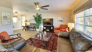 A living room with leather sofas, a coffee table, a TV, and a ceiling fan. - Waterfront Home w/ Boat Dock & Bar in N Fort Myers (North Fort Myers)