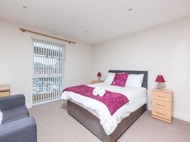 A bedroom with a bed, two bedside tables, a chair, and a window with blinds.