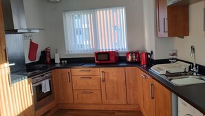 A compact kitchen with wooden cabinets, a black countertop, a microwave, a toaster, and a sink. - Marina View Apartment (Swansea)