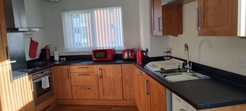 A compact kitchen with wooden cabinets, a black countertop, a microwave, a toaster, and a sink.