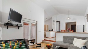 A living room with a foosball table, a sofa, a television, and a kitchen area in the background. - Kuća za odmor Barbariga-Betiga (Vodnjan)