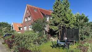 Une maison avec un toit rouge, un jardin avec un trampoline et une voiture garée dans la rue.