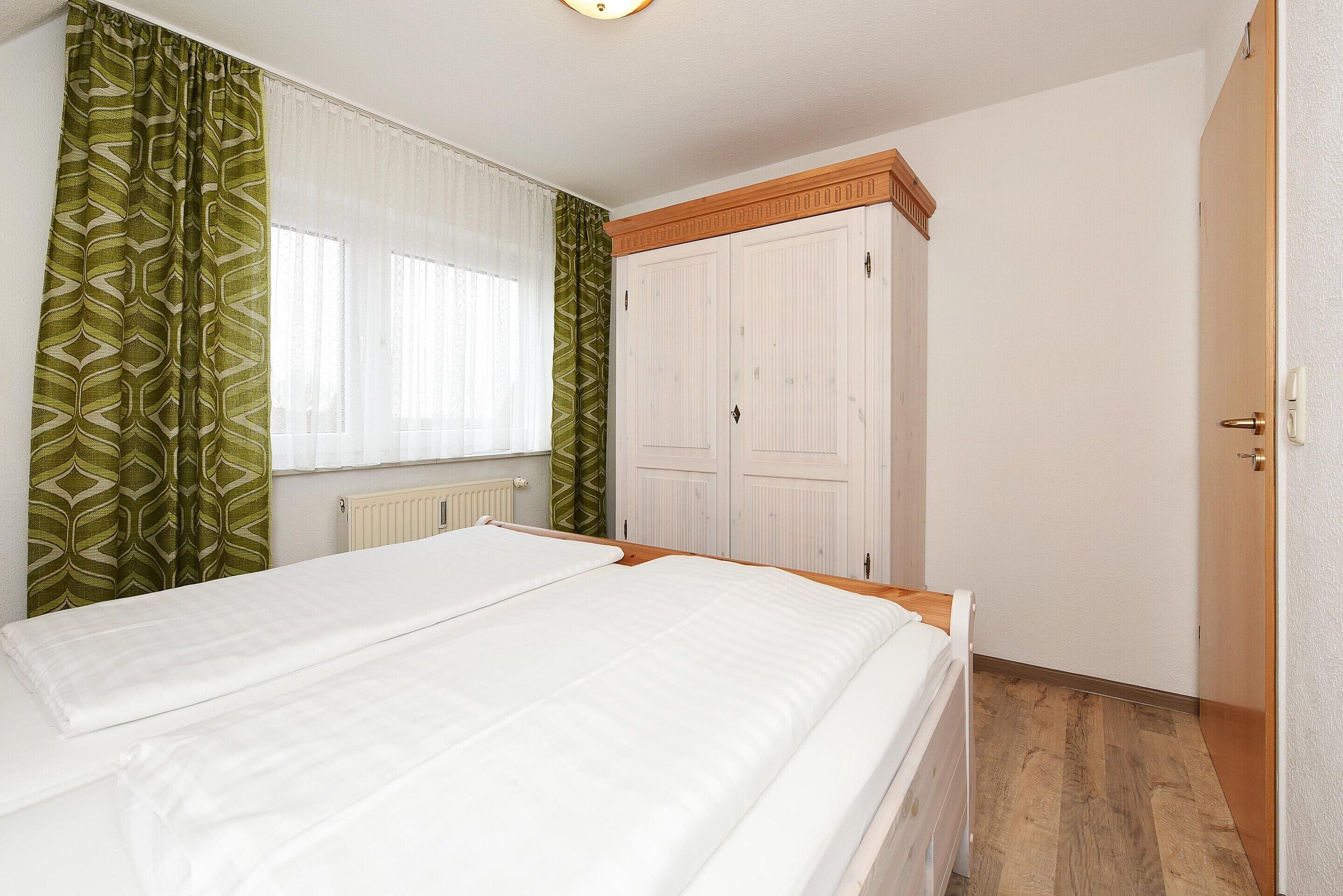 Une chambre à coucher avec un lit, une armoire et une fenêtre avec des rideaux.