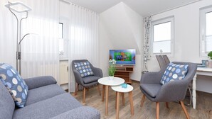 Un salon moderne avec des canapés gris, une petite table blanche et un téléviseur fixé au mur.
