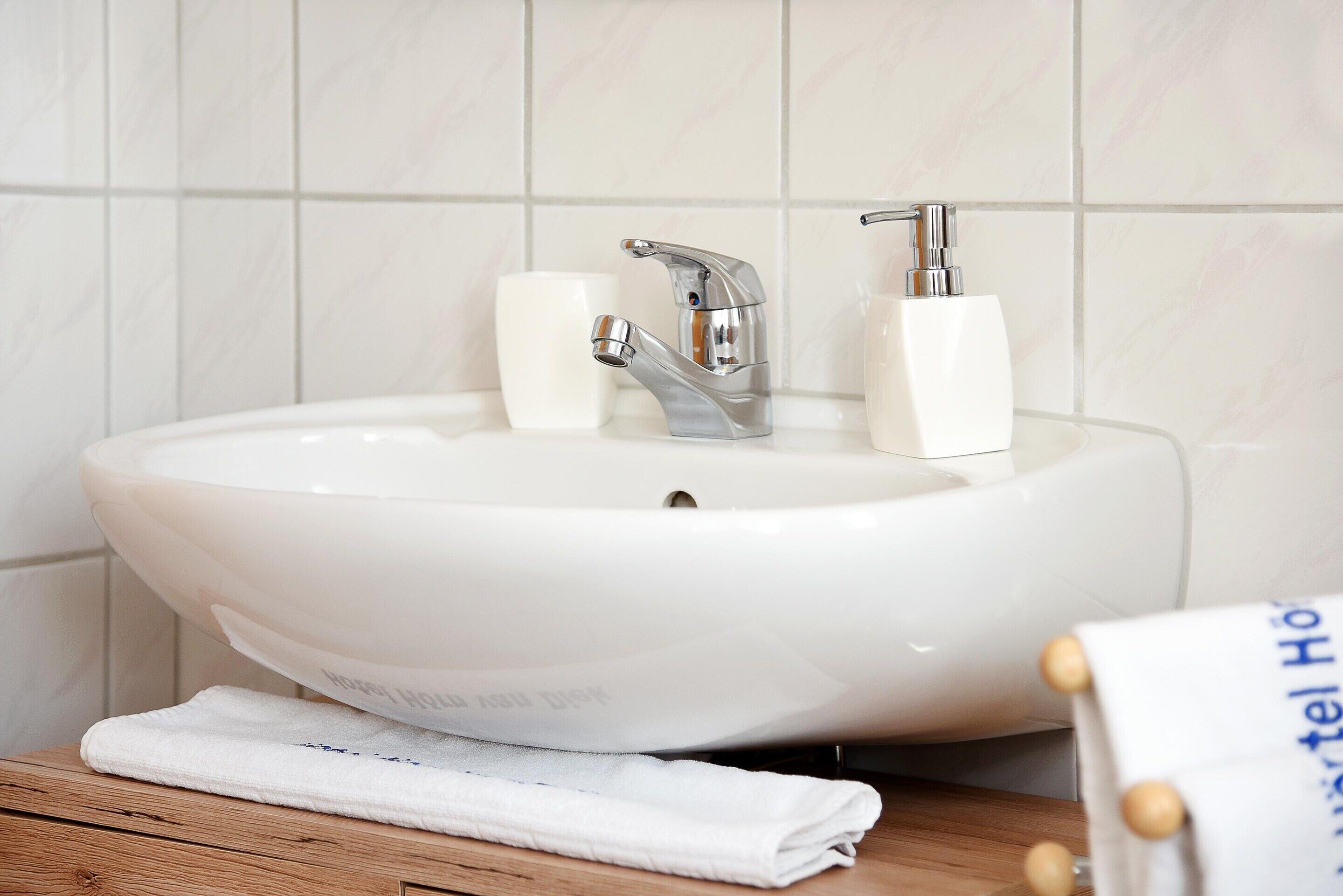 A white bathroom sink with a modern faucet, a soap dispenser, and a towel on a wooden surface.