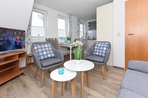 Una sala de estar moderna con dos sillones grises, una mesa de centro blanca y un mueble para televisión.