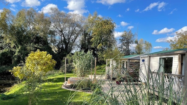 A mobile home with a fenced yard, a small pond, and surrounding trees. - BLUE GRASS RANCH - MOBILE HOME YUCCA & JACUZZI (Bischoffsheim)