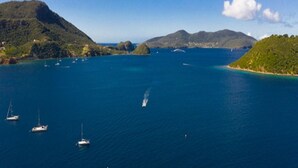 A coastal landscape with clear blue waters, several sailboats, and green hills.