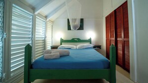 A bedroom with a bed, white curtains, a hanging light fixture, and wooden shutters.