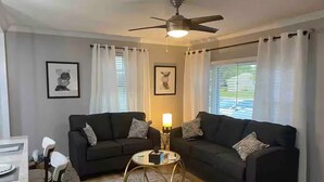 Ein Wohnzimmer mit zwei schwarzen Sofas, einem runden Couchtisch und einem Deckenventilator.