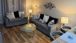 Ein modernes Wohnzimmer mit zwei grauen Sofas, einem Glastisch und einem Deckenventilator.