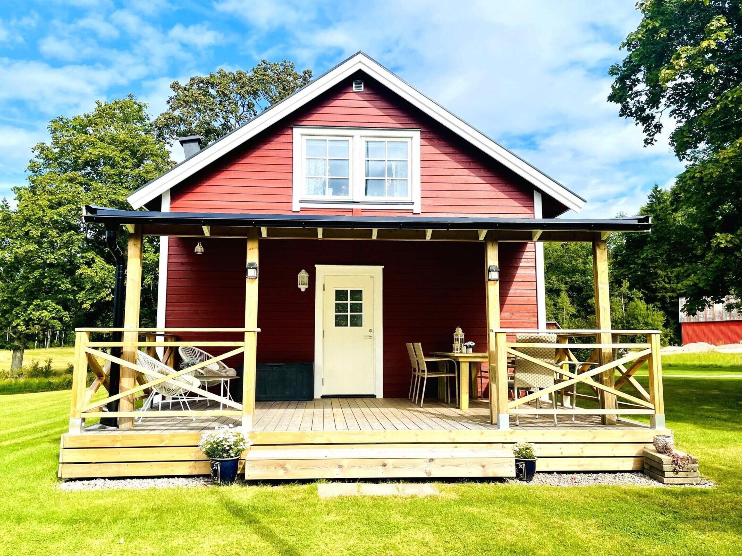 A red wooden house with a porch, a door, and a window.