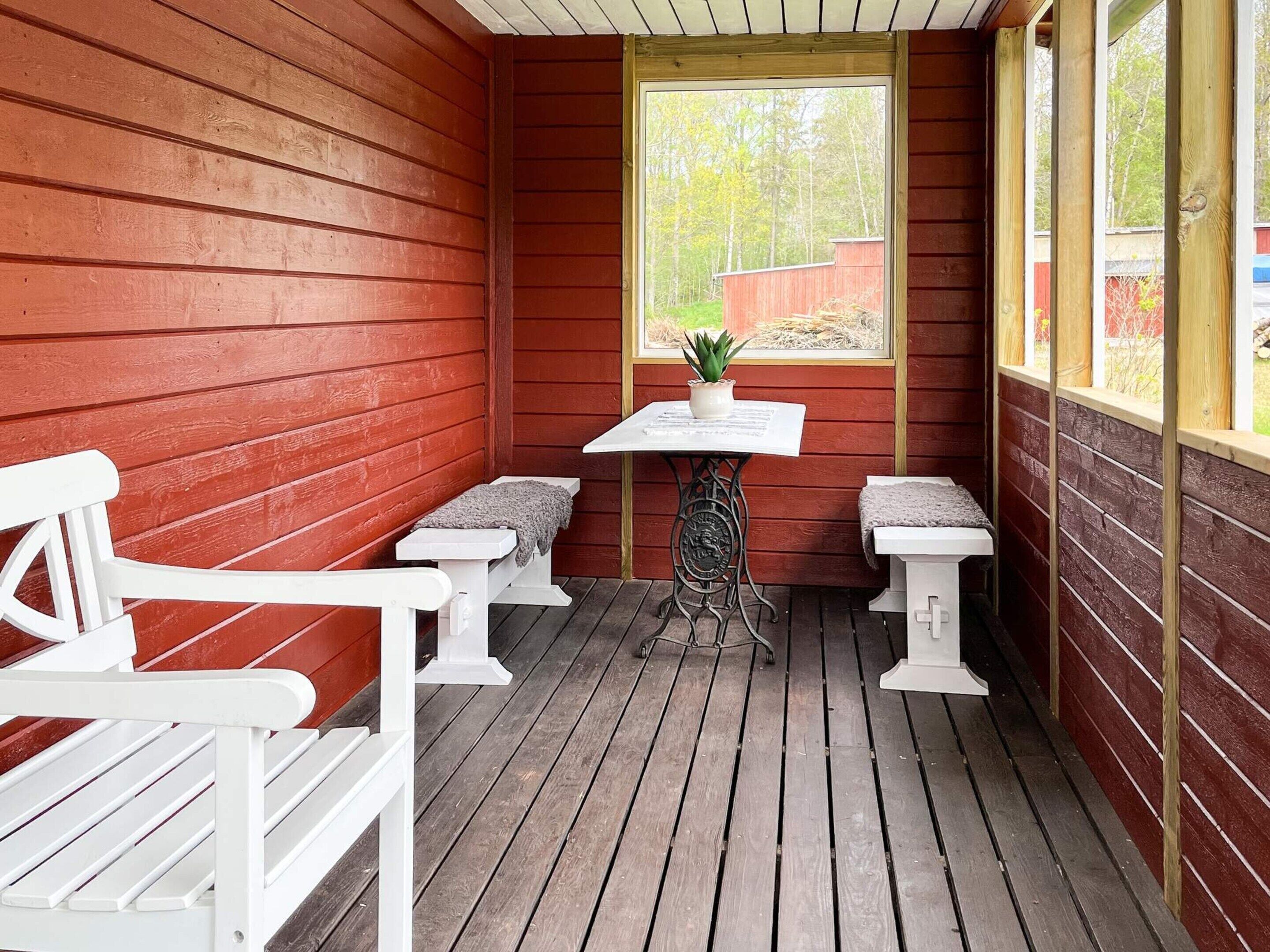 Un'area esterna con un pavimento in legno, panchine e un tavolo, una finestra vista alberi e una pianta in vaso sul tavolo.