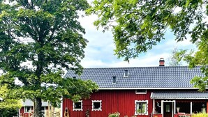 A red barn with a grey roof, surrounded by green grass and trees. - 4 Star Holiday Home in Bralanda (Bralanda)