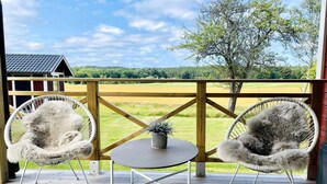 A wooden deck with two white wicker chairs and a small round table, overlooking a grassy field and a distant building. - 4 Star Holiday Home in Bralanda (Bralanda)