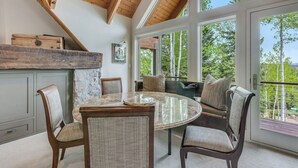 A dining area with a round table and chairs, a stone wall, and a view of trees through large windows. - The Silos by Snowmass Vacations (Snowmass Village)