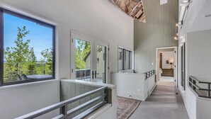 A modern interior with a staircase leading to a second floor, large windows offering a view of trees, and a patterned rug on the floor. - The Silos by Snowmass Vacations (Snowmass Village)