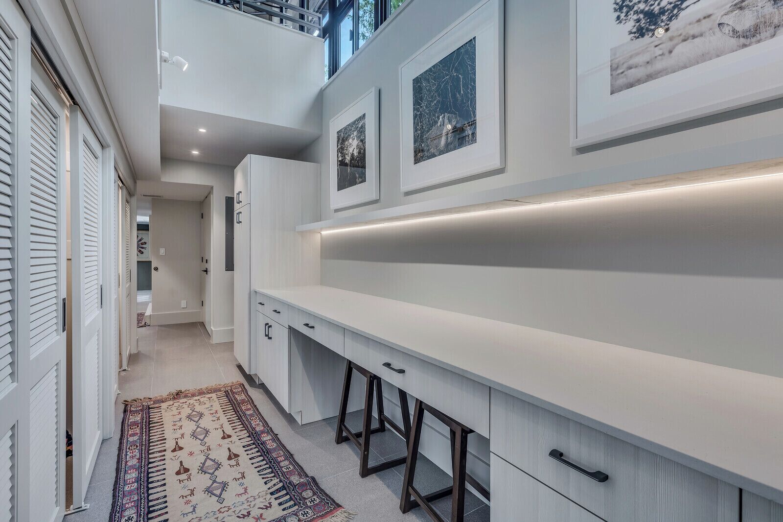 A modern kitchen with white cabinetry, a long countertop, and a decorative rug.