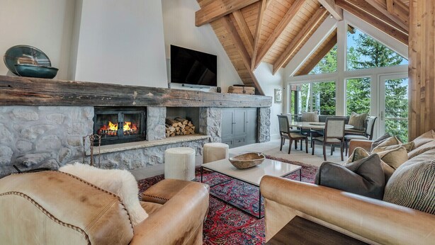 A cozy living room with a stone fireplace, wooden beams, and a large window overlooking greenery. - The Silos by Snowmass Vacations (Snowmass Village)