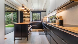 A modern kitchen with a large island, black cabinetry, and a view of a garden through the window. - Villa 243 - Charming Villa in a peaceful area (Orbacém)