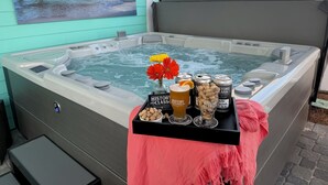 A hot tub with a pink towel, a tray with drinks and snacks, and a painting of a pier.