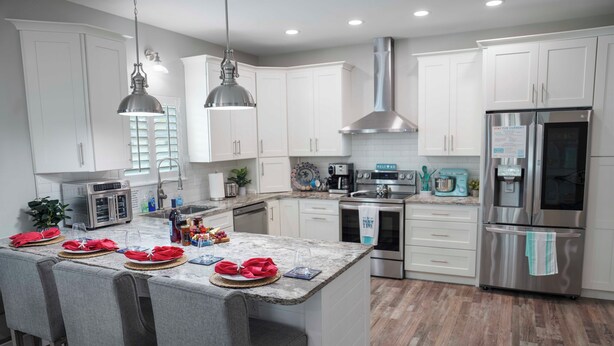 A modern kitchen with white cabinets, stainless steel appliances, and a marble island with seating.