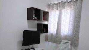 Un salon doté d’un téléviseur à écran plat, de meubles blancs et d’une fenêtre avec des rideaux.