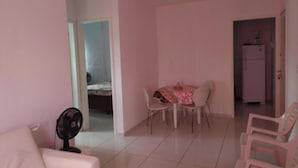 Une pièce aux murs roses, une table à manger avec des chaises, un ventilateur et un réfrigérateur à l’arrière-plan.