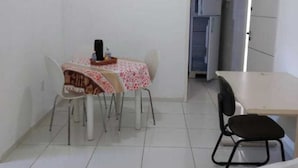 Une petite pièce propre, comprenant une table et des chaises, un coin cuisine et une porte donnant sur une autre pièce.
