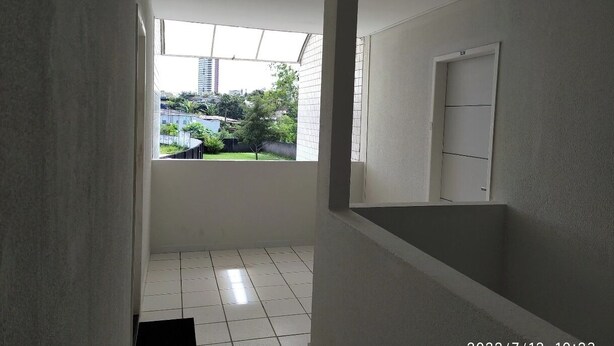 Un couloir étroit avec une fenêtre donnant sur un balcon, des murs blancs et un sol carrelé.