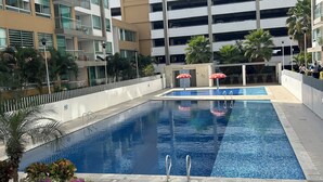 A swimming pool with a tiled deck, surrounded by a low fence and palm trees. - Charming 2-bedroom apartment in delightful Barranquilla with AC (Barranquilla)