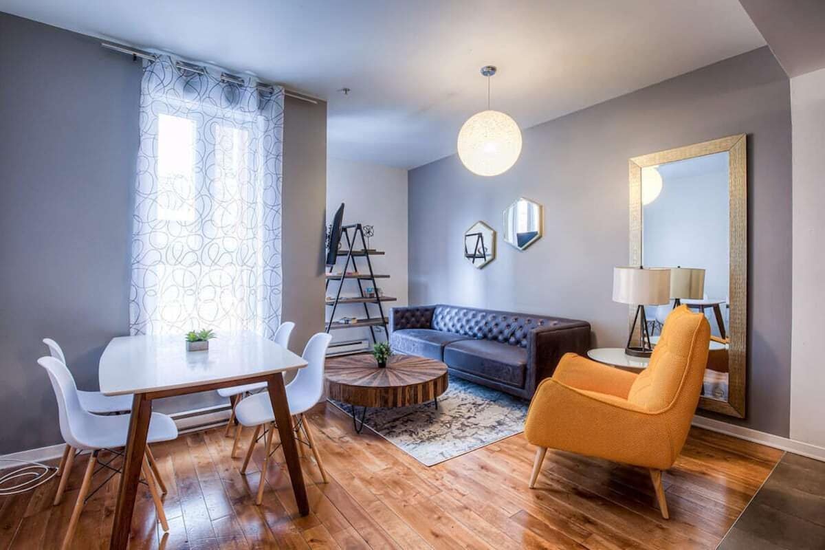 Un salon moderne comprenant une table à manger, un canapé et un fauteuil, une échelle et un grand miroir.