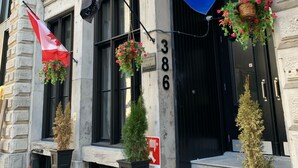 A building with a black door, numbered 386, and two potted plants on the steps. - Le Moyne-Heritage  (Montréal)