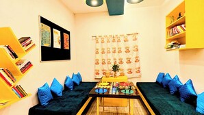 A room with two yellow sofas, a central table with a board game, and bookshelves on the walls. - Hidden Monkey Hostel Chet Singh Ghat (Varanasi)