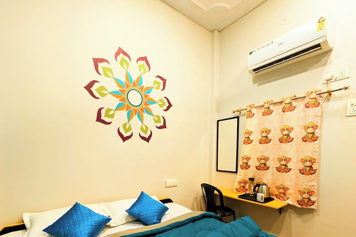 A hotel room with a bed, a desk, an air conditioner, a wall decoration, and a shower curtain with a monkey design.