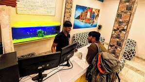 A reception desk with a computer, a whiteboard with information, and a mural on the wall. - Hidden Monkey Hostel Chet Singh Ghat (Varanasi)