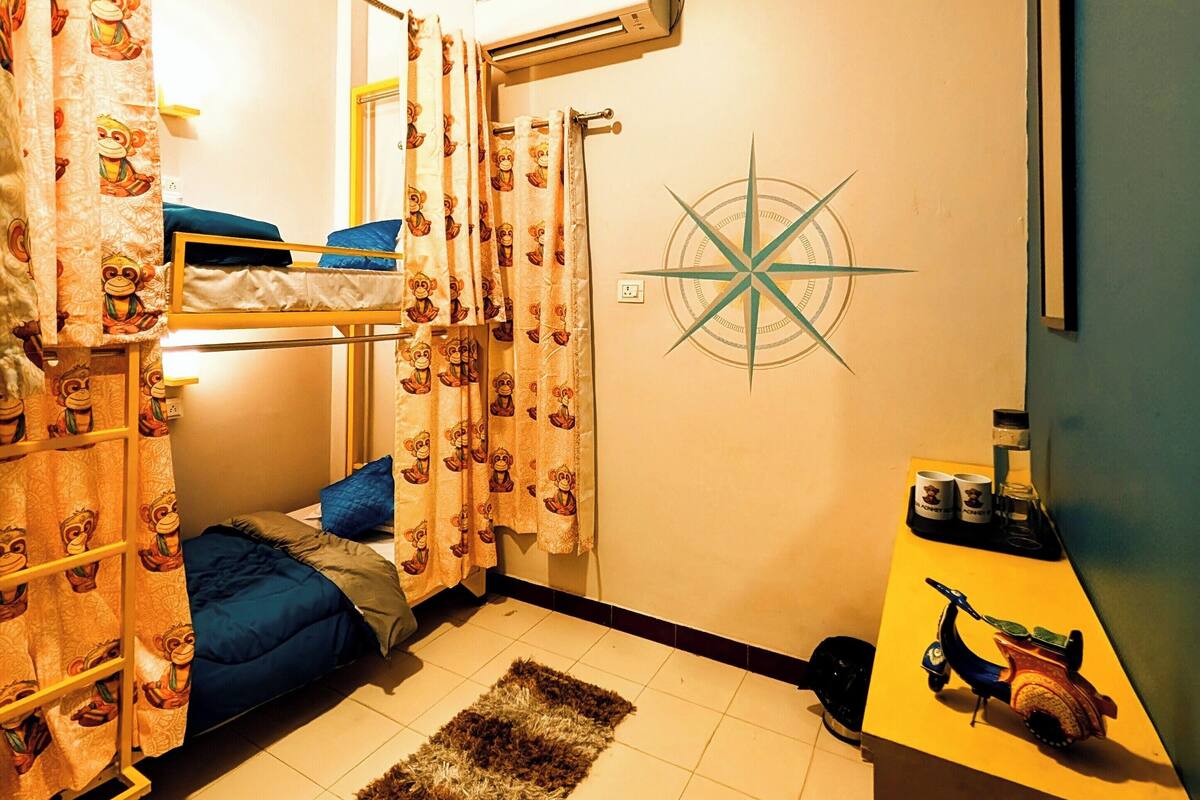 A dormitory room with bunk beds, a small desk, a coffee maker, and a compass decoration on the wall.