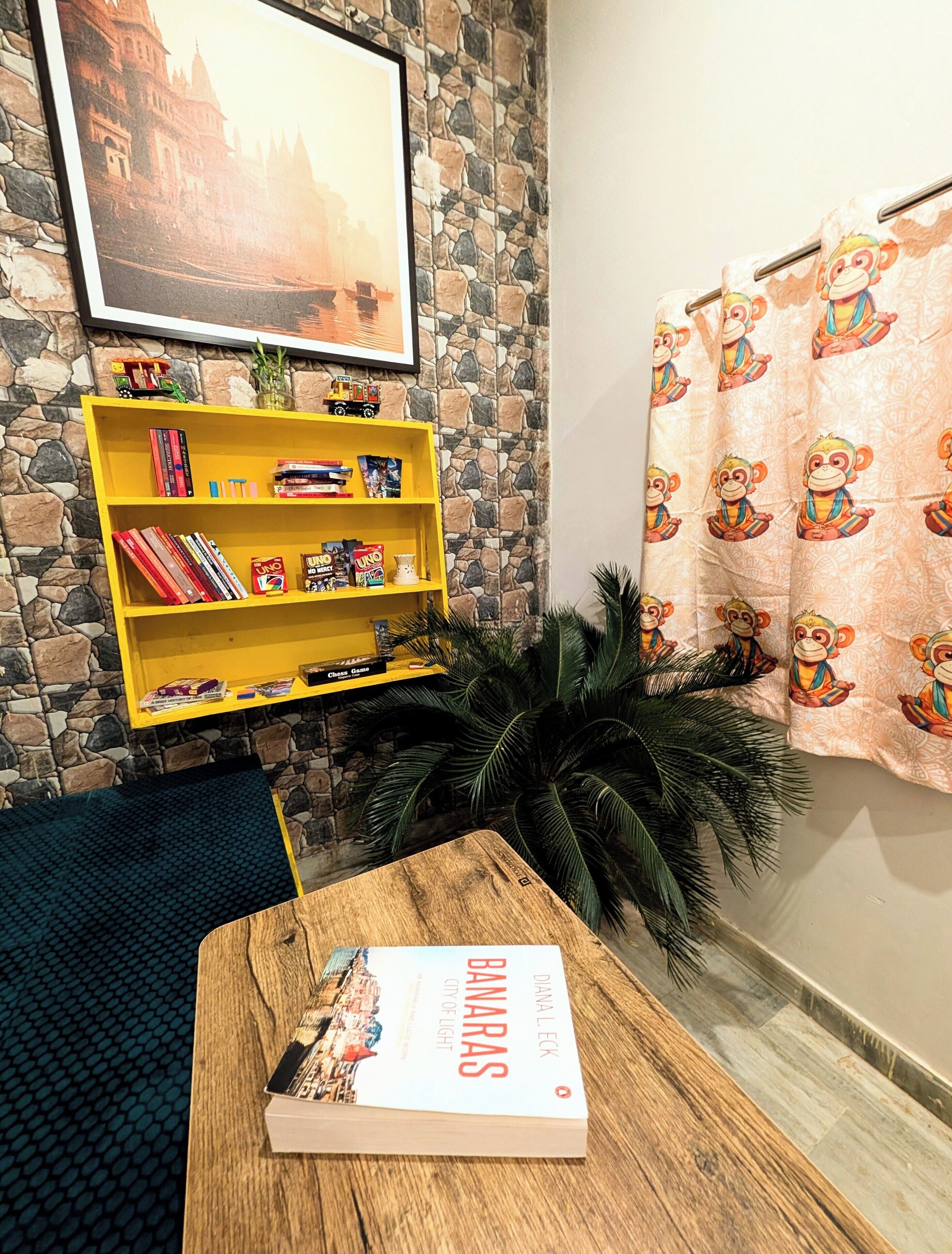 A room with a wooden table, a yellow bookshelf, a framed picture on the wall, and a curtain with monkey prints.