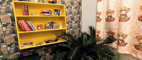 A room with a wooden table, a yellow bookshelf, a framed picture on the wall, and a curtain with monkey prints.