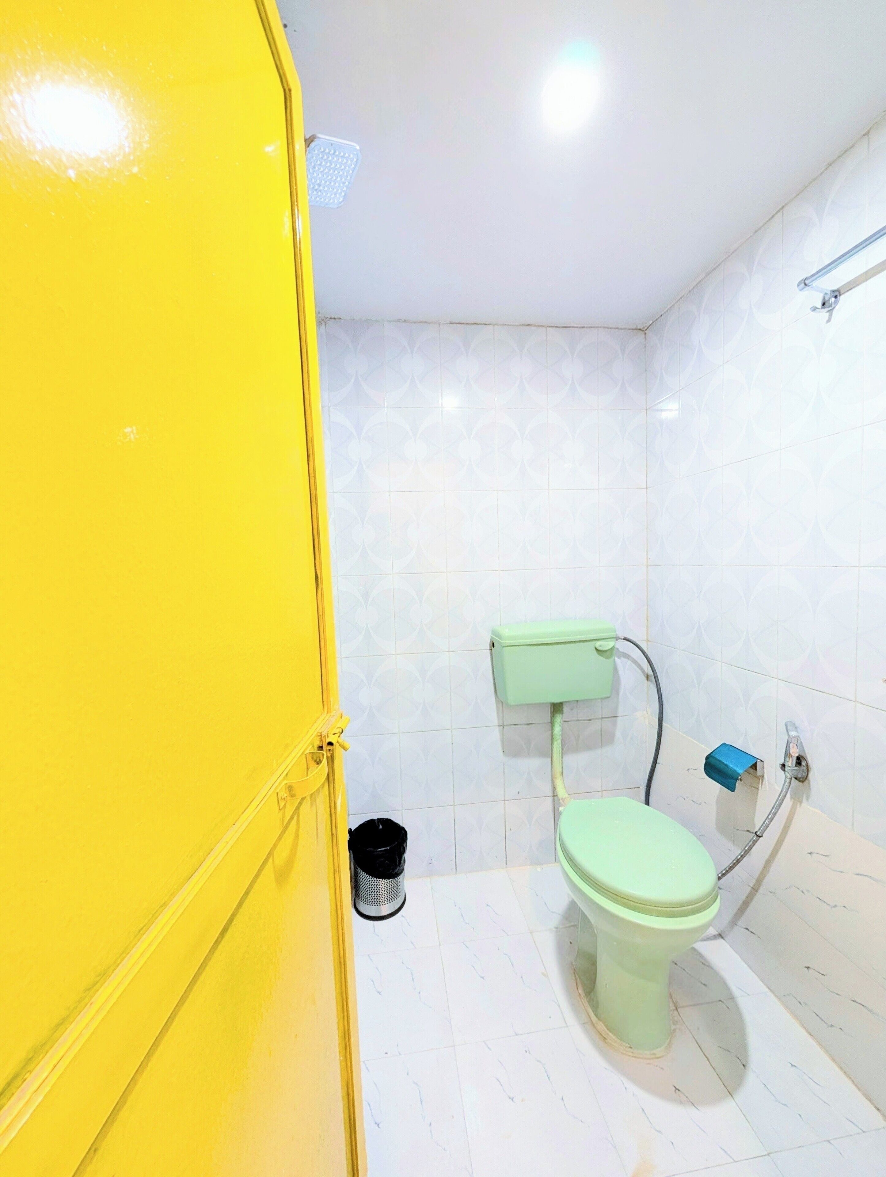 A small, compact bathroom with a toilet, a trash bin, and a shower area.
