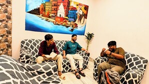 A room with three black and white patterned sofas, a large painting of a cityscape, and a stone wall. - Hidden Monkey Hostel Chet Singh Ghat (Varanasi)
