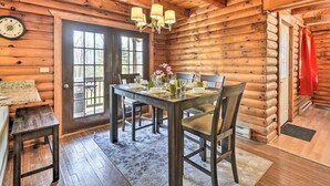 A wooden cabin interior with a dining table set for four, a chandelier, and a clock on the wall. - Calming Retreat · Cozy Poconos Cabin (Pleasant Mount)