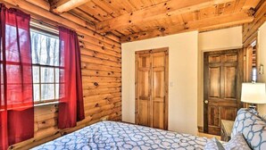 Camera da letto in legno tipica di una baita, con un letto, pareti in legno, una finestra con tende e una porta.