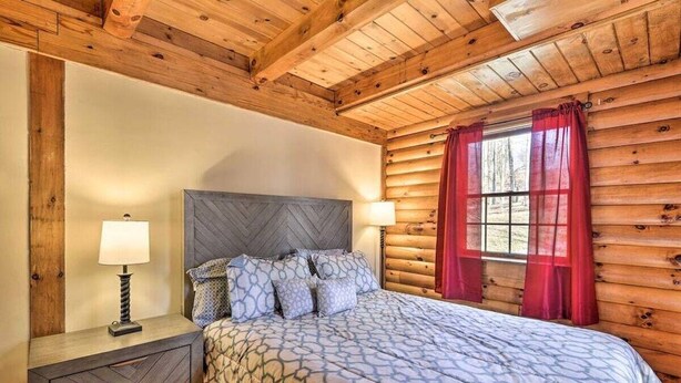 A wooden cabin bedroom with a bed, two bedside tables, and a window with curtains. - Calming Retreat · Cozy Poconos Cabin (Pleasant Mount)