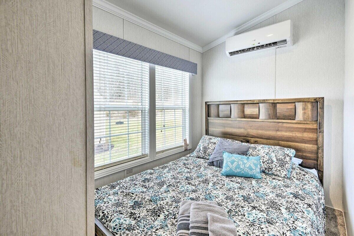 Ein Schlafzimmer mit Bett, Jalousien, einer Klimaanlage und einem hölzernen Kopfteil.